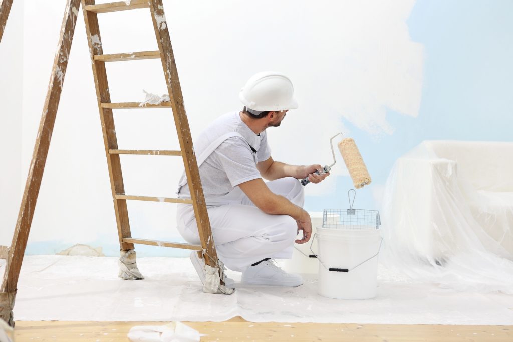 Painter man at work takes the color with paint roller from bucket